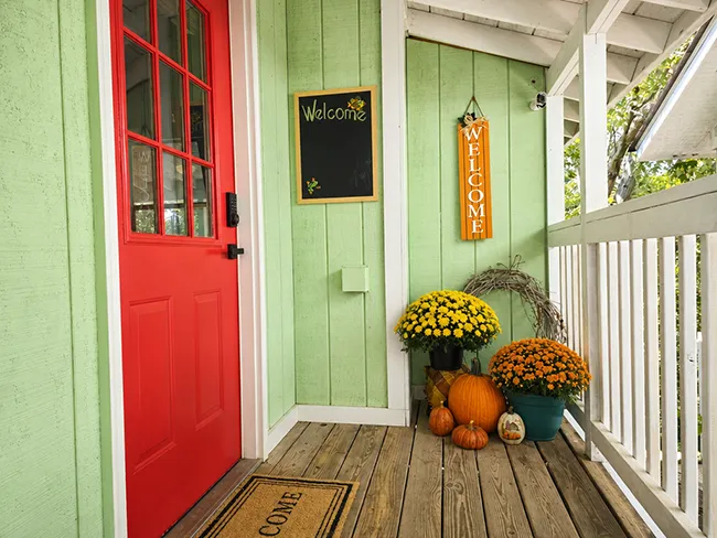 Covered front porch with the red front door, a welcome chalkboard, and a grapevine wreath