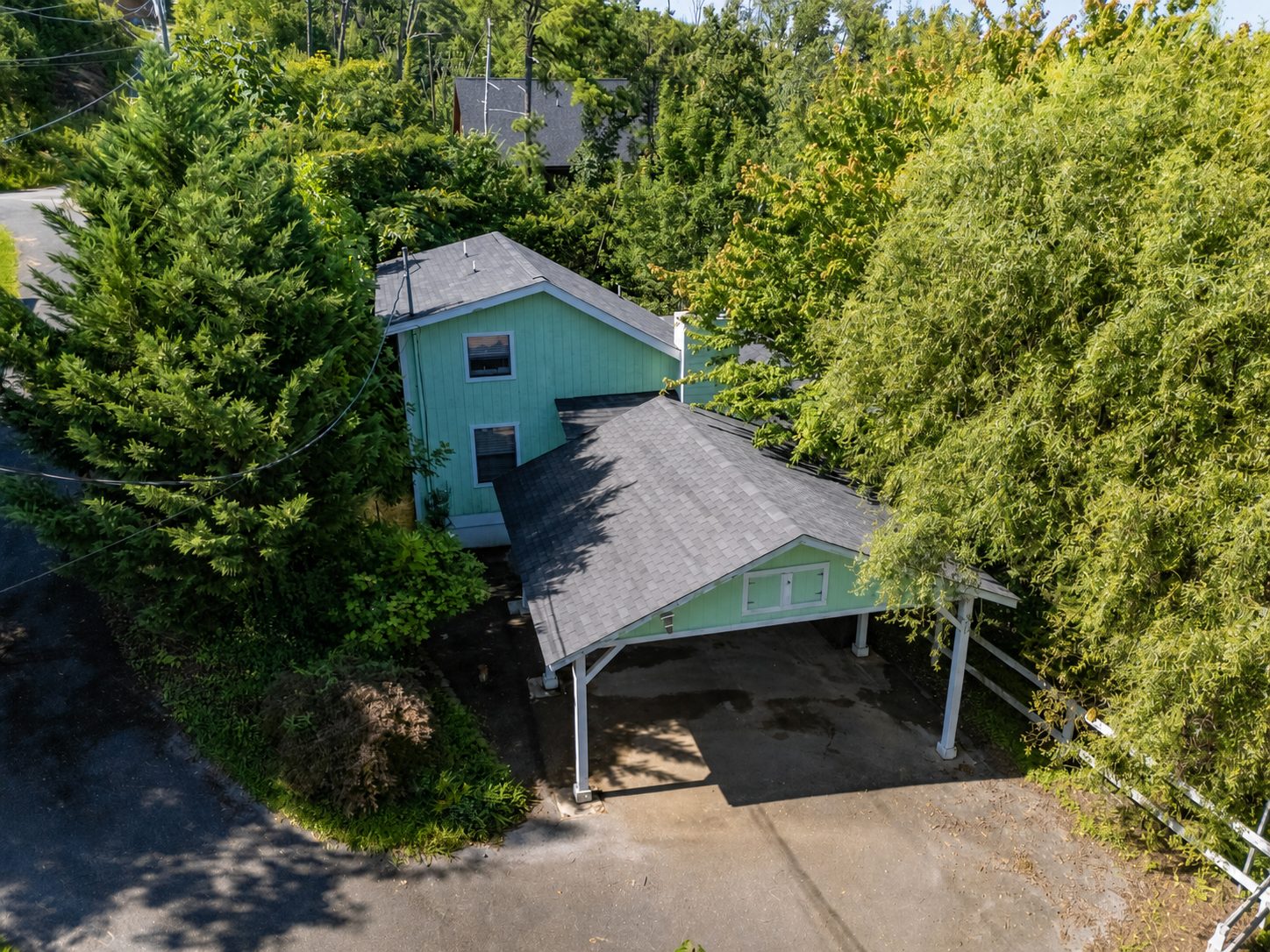 Willow Ridge Cottage seen from above, mint green siding and a carport, surrounded by wooded hills