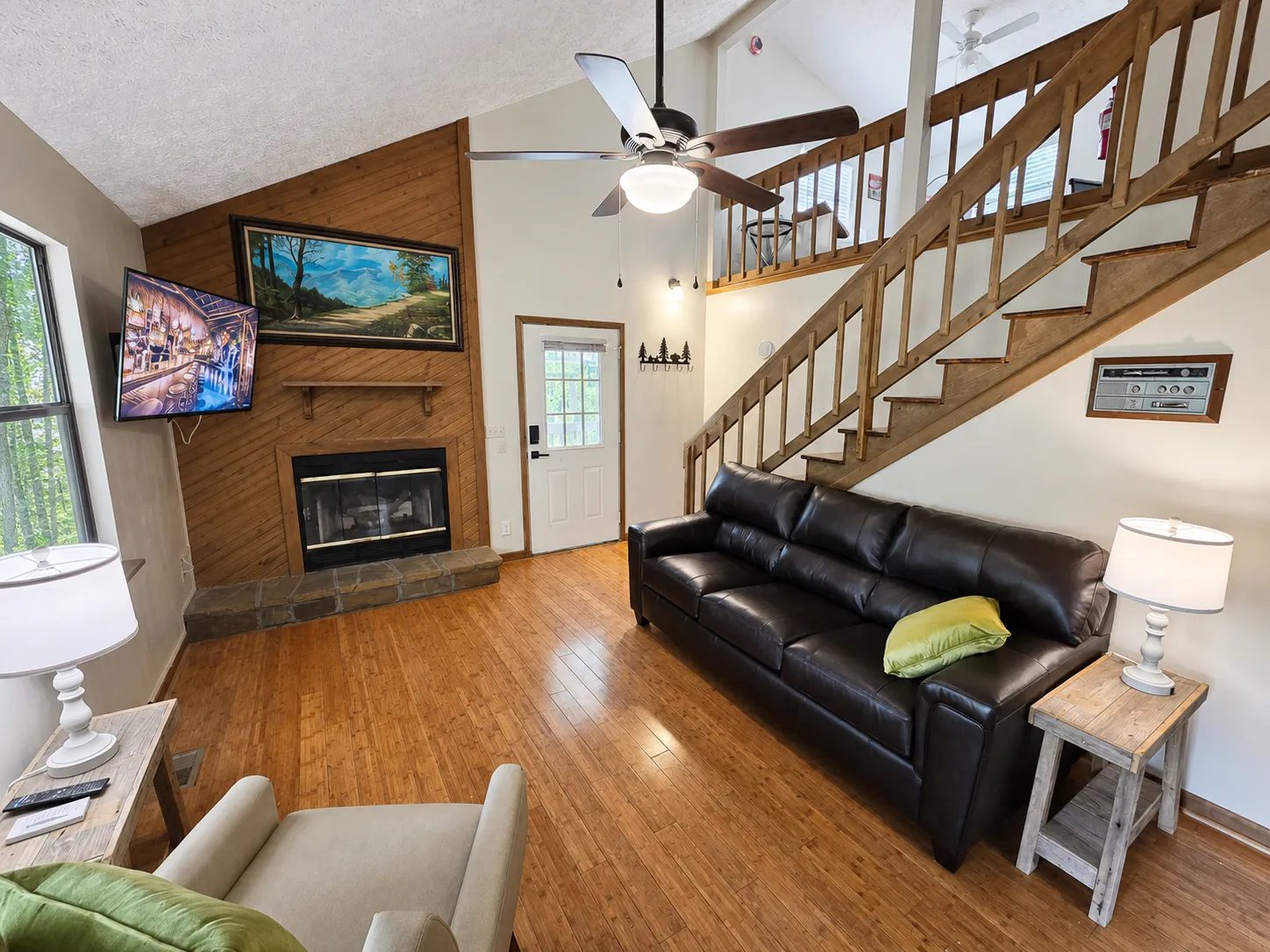 Living room with the stone fireplace, vaulted ceiling, and stairs to the loft